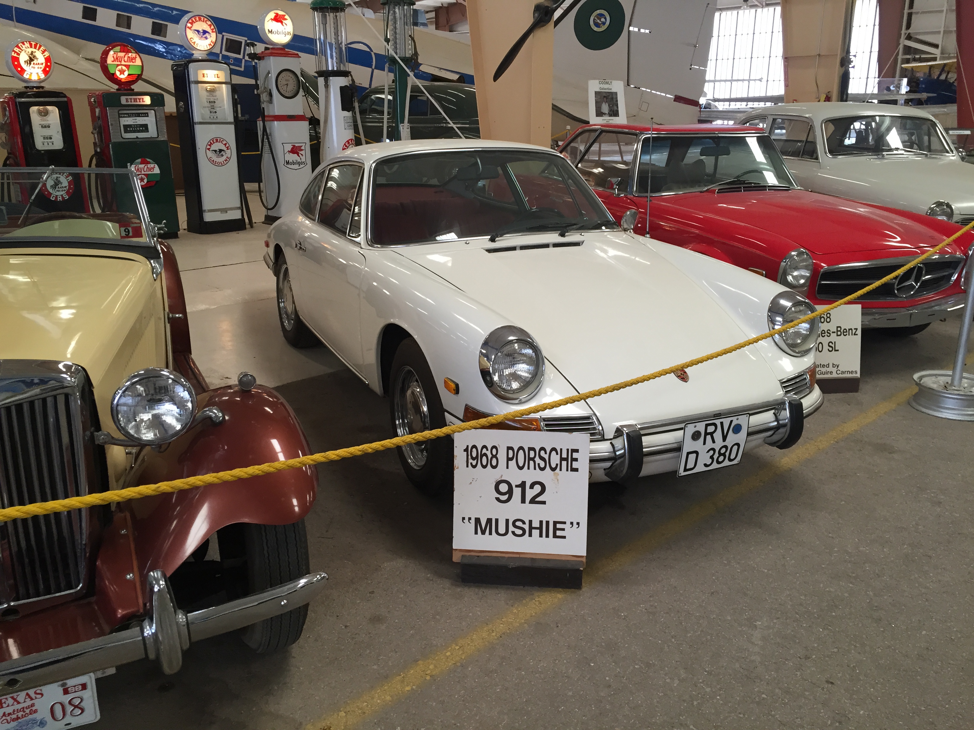 A Porche and a Mercedes-Benz. Behind these cars there are the vintage gas pumps.